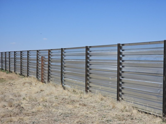 A long metal fence stretches across a dry area.