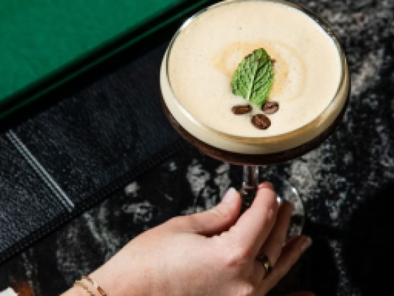 Hand holding a latte cocktail on a dark table