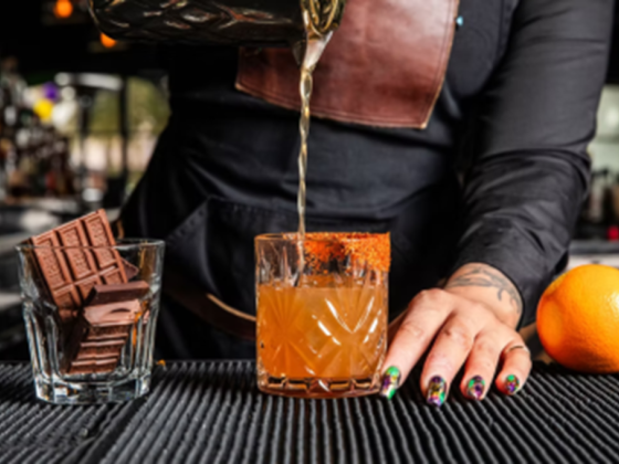 Bartender mixes drink with chocolate and orange on bar