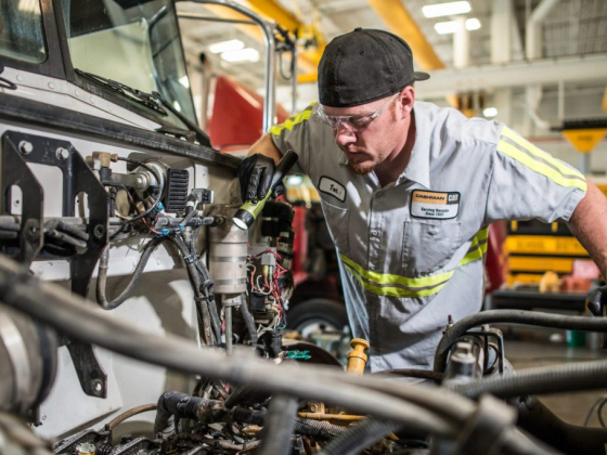 A mechanic examines vehicle wiring in a workshop setting.