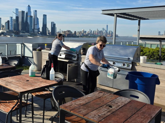 Workers clean BBQ on a patio with city skyline view