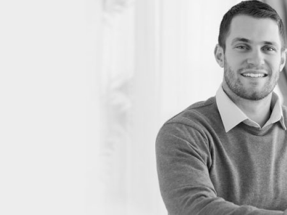 Man smiling at desk with a laptop in monochrome