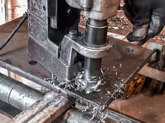 Drill press creating hole in metal sheet with operator's hand