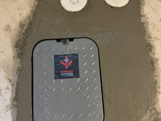 Gray access panel with 'Tornado Plumbing' logo on concrete
