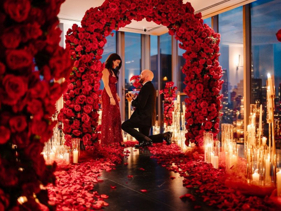 Man on knee proposing to woman under rose arch