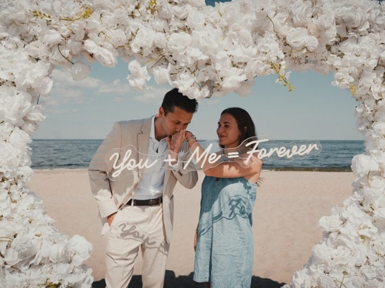 A couple shares a moment on a beach, under a flower arch.