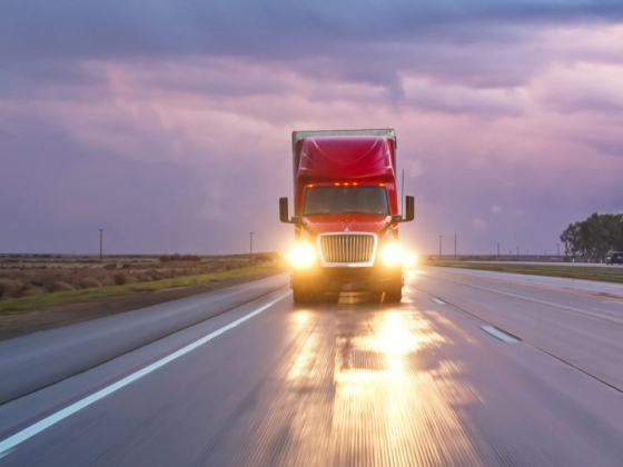 A semi-truck travels along a deserted highway at dusk