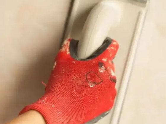 Red-gloved hand smoothing a wall with a tool