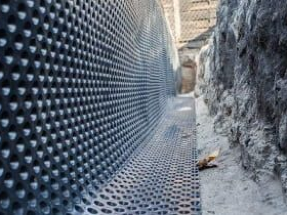 Dimpled sheet lining a trench beside a stone wall