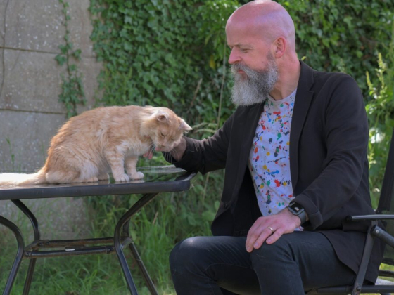 A bearded man gently pets a cat on a sunny day