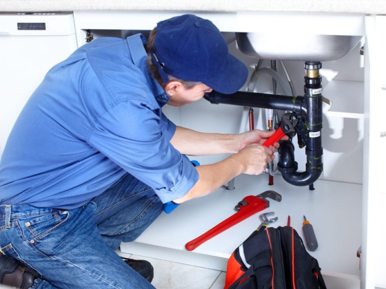 Plumber repairing pipes with a wrench under a kitchen sink