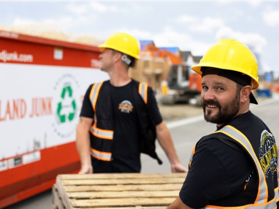 Two workers carry a wooden pallet at a construction site
