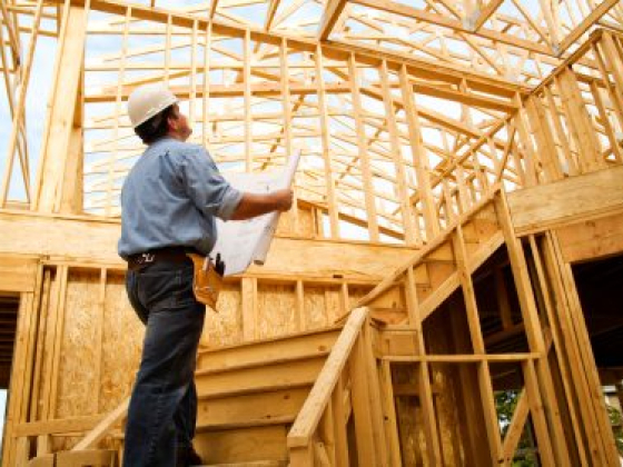 Worker inspects house frame with blueprint in hand