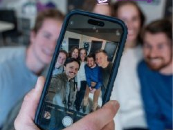 Friends smiling for a group selfie using a phone