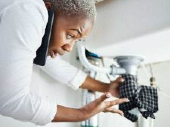 Woman under sink repairing a leak with phone support