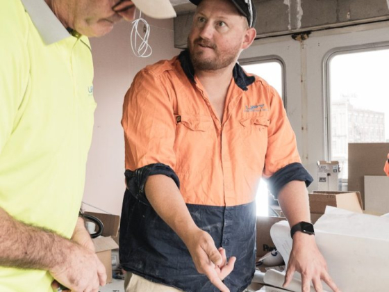 Workers collaborate over construction blueprints indoors