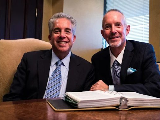 Two businessmen seated at a desk with open binder