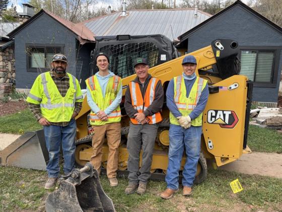 Four workers pose in front of heavy equipment