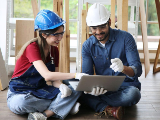 Workers in helmets discussing a project on their laptop.