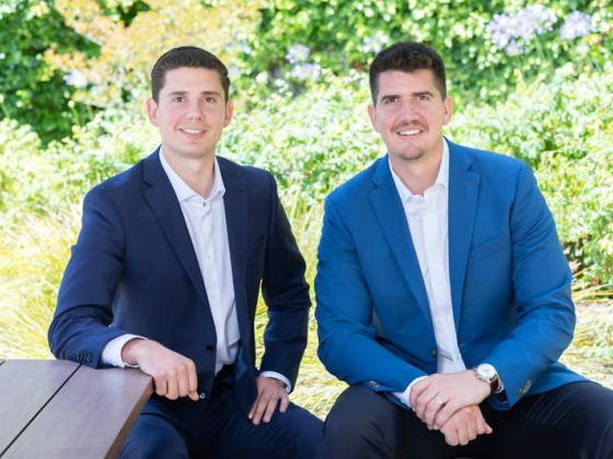 Two men smiling, seated outside surrounded by greenery
