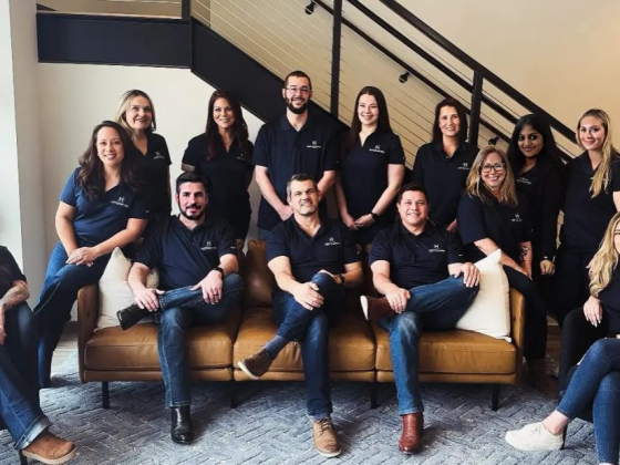 A group of coworkers in matching shirts seated and standing on a sofa