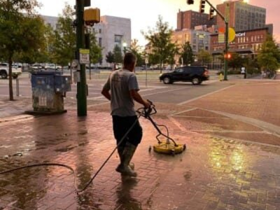 City worker power washes sidewalk in urban area, sunset in background