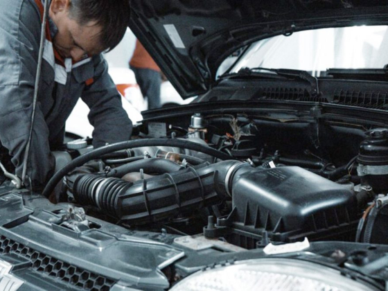 A mechanic works on an engine under the car's hood