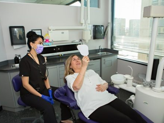 Woman checks smile with mirror at dentist's office