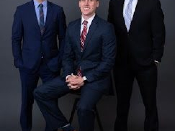 Three men smiling in suits against a gray backdrop