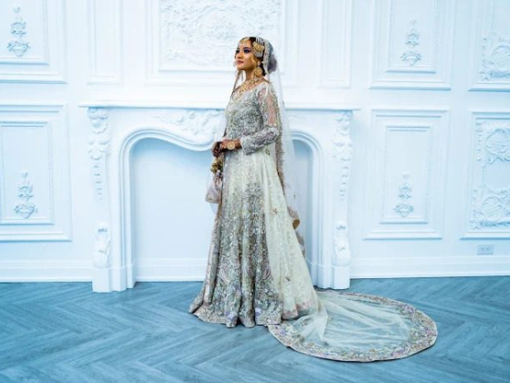 Bride in elegant, detailed wedding dress beside white ornate wall