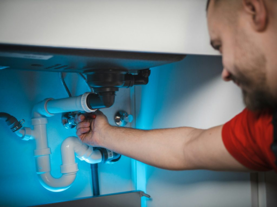 A plumber adjusts sink pipes in a kitchen