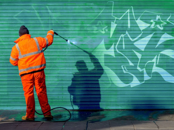 Man in orange suit cleaning graffiti with high-pressure washer