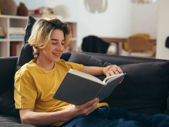Smiling individual enjoying a book on a sofa