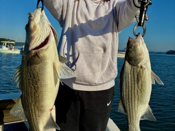 Smiling person displays two catches on a sunny lake