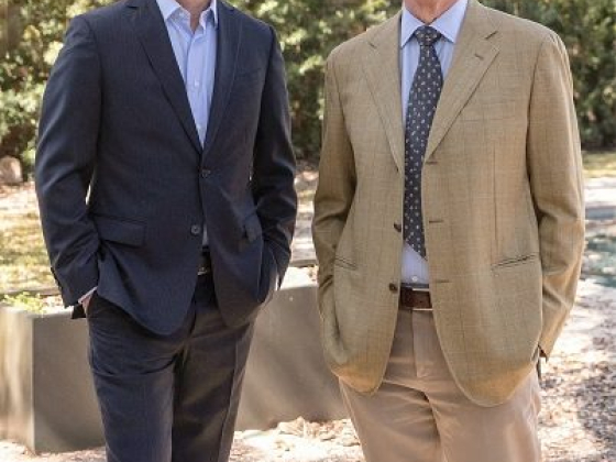Two men smile while posing outside in formal attire