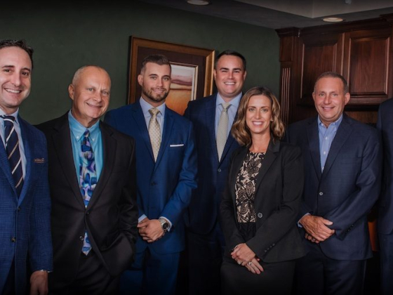 Seven individuals dressed in suits and smiles