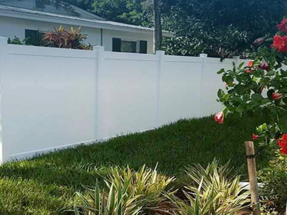 A white fence borders a lush garden with red flowers.