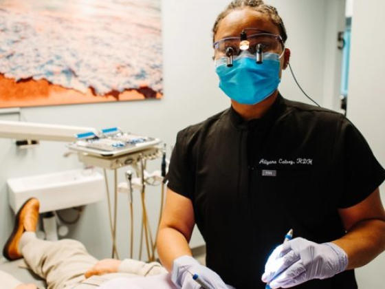 Hygienist wearing mask and gloves checks patient's teeth