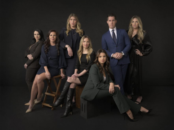 A group portrait of seven people in formal attire against a dark background