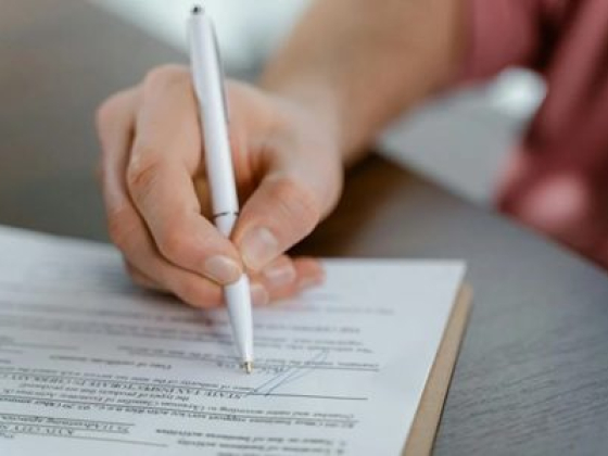 Close-up of hand signing a form with a pen