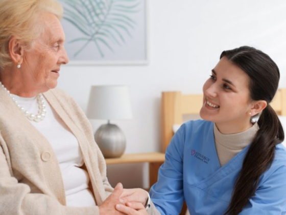 Smiling nurse in blue talks with senior in cozy room