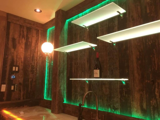 Illuminated shelves on wooden wall display a wine bottle
