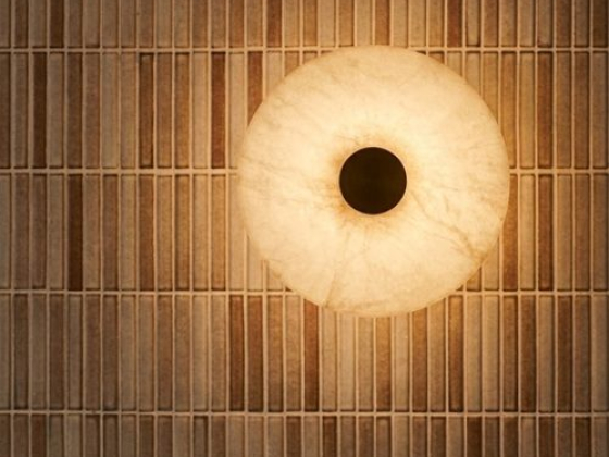 A round light fixture illuminates textured wall tiles.