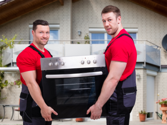 Two men in red shirts moving an oven outside a home