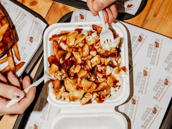 Two people sharing poutine on a wooden table